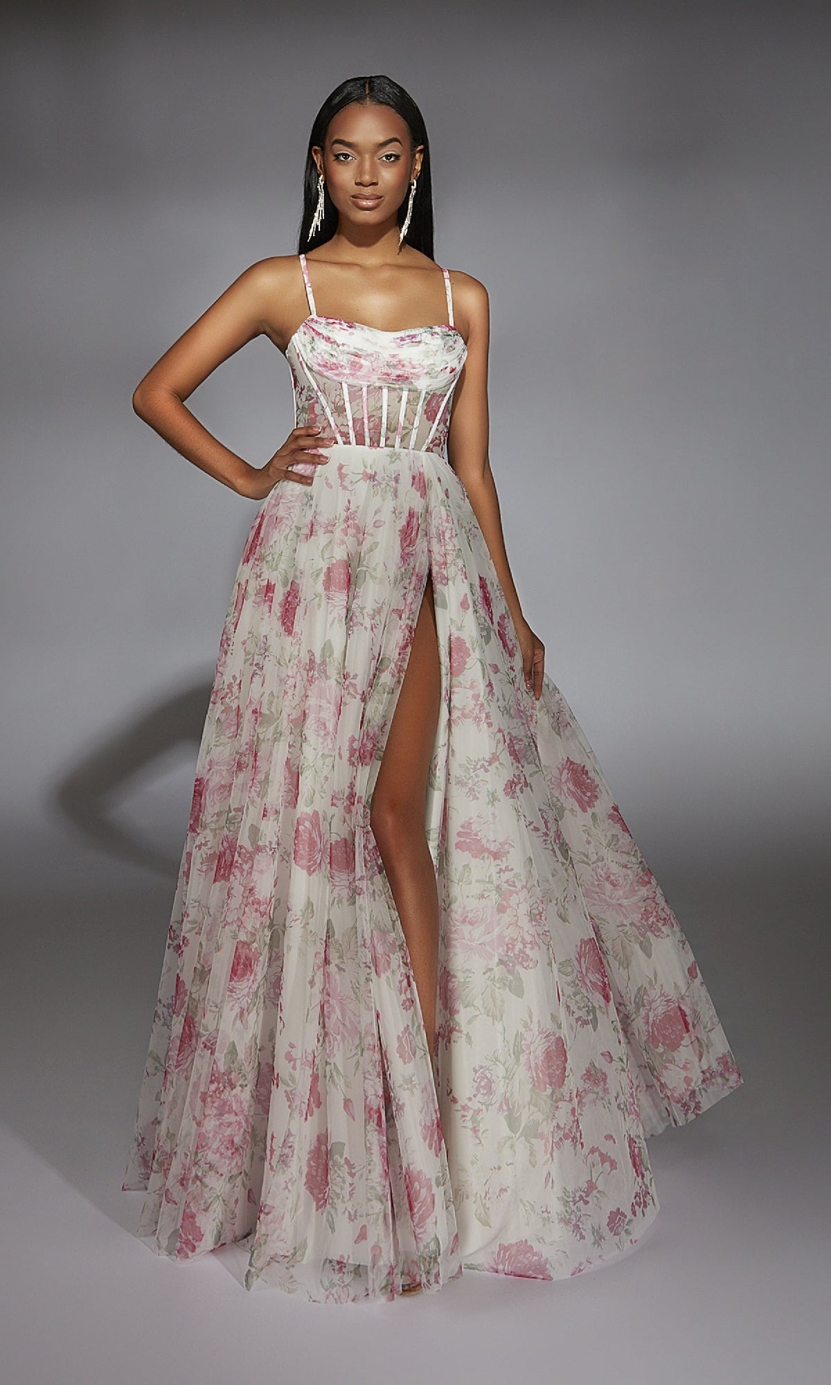 A woman models the Alyce 61752 long prom dress with a sheer corset bodice, printed fabric, and a high slit, standing against a plain gray background.